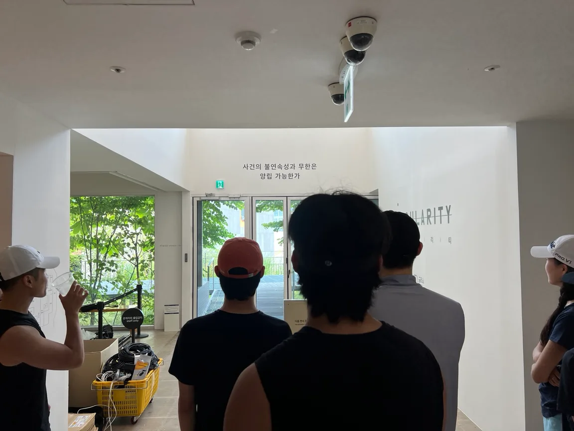 A group of PMCC members stands together inside an exhibition space, looking at the exhibition’s opening question.